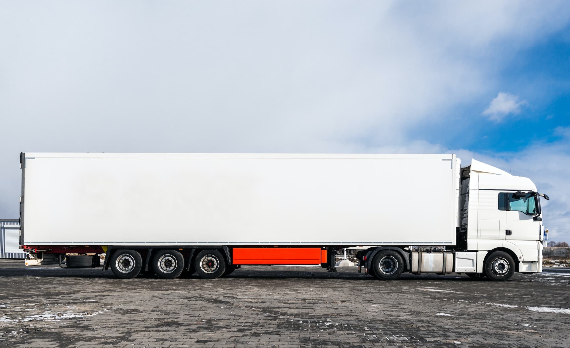 A big white truck with a white trailer standing on the countryside road in against a blue sky