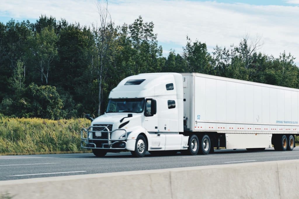 All white tractor trailer driving on a highway transporting and delivering goods and shipments