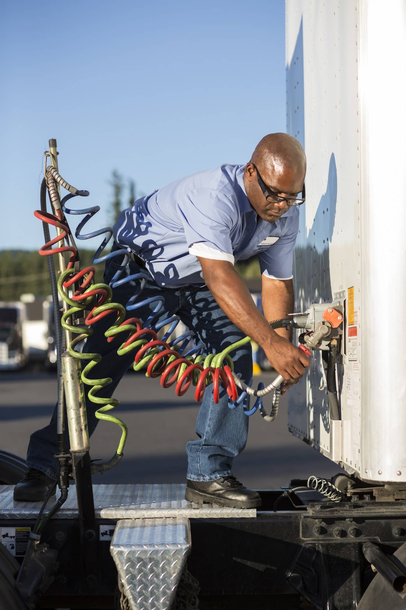 Truck driver attaching power cables from truck tractor to trailer at a truck stop.