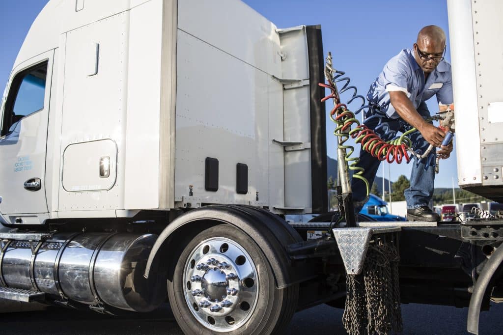 Truck driver attaching power cables from truck tractor to trailer at a truck stop.