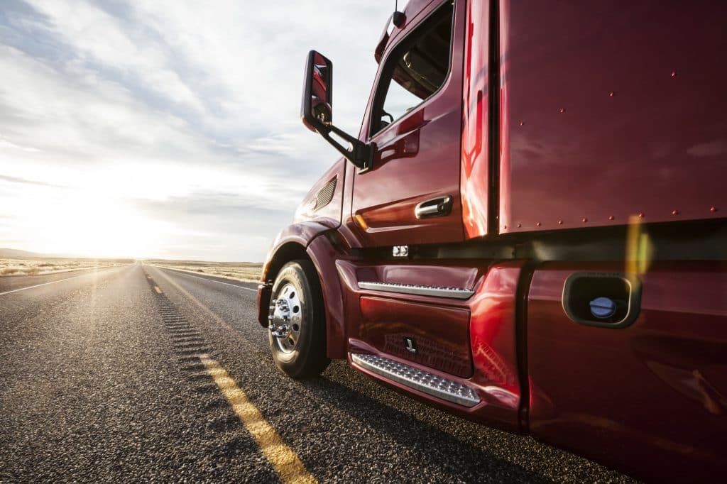 Close up side view looking forward of a commercial truck on a highway at sunset.