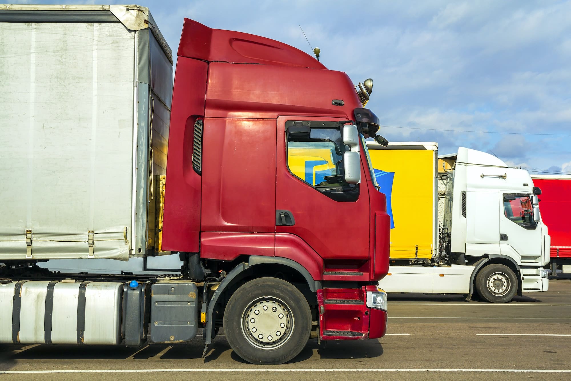 Colorful modern big semi-trucks and trailers of different makes and models stand in row on flat