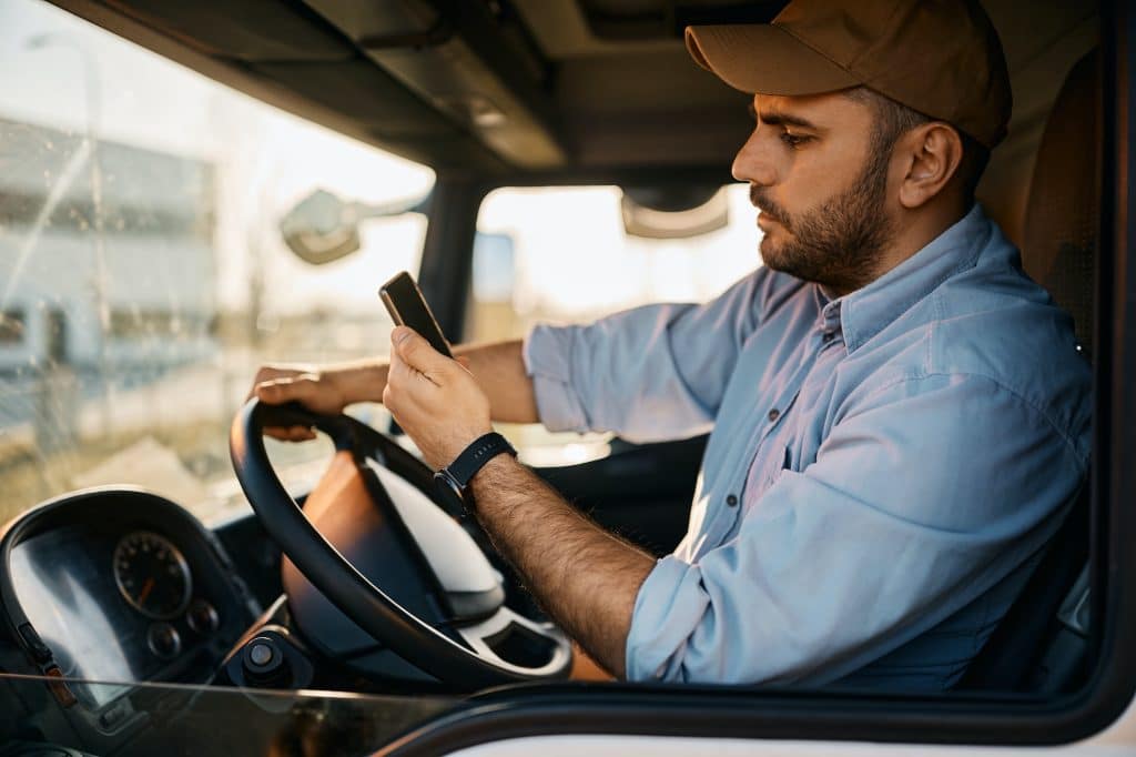 Side view of truck driver reading text message on smart phone while driving.