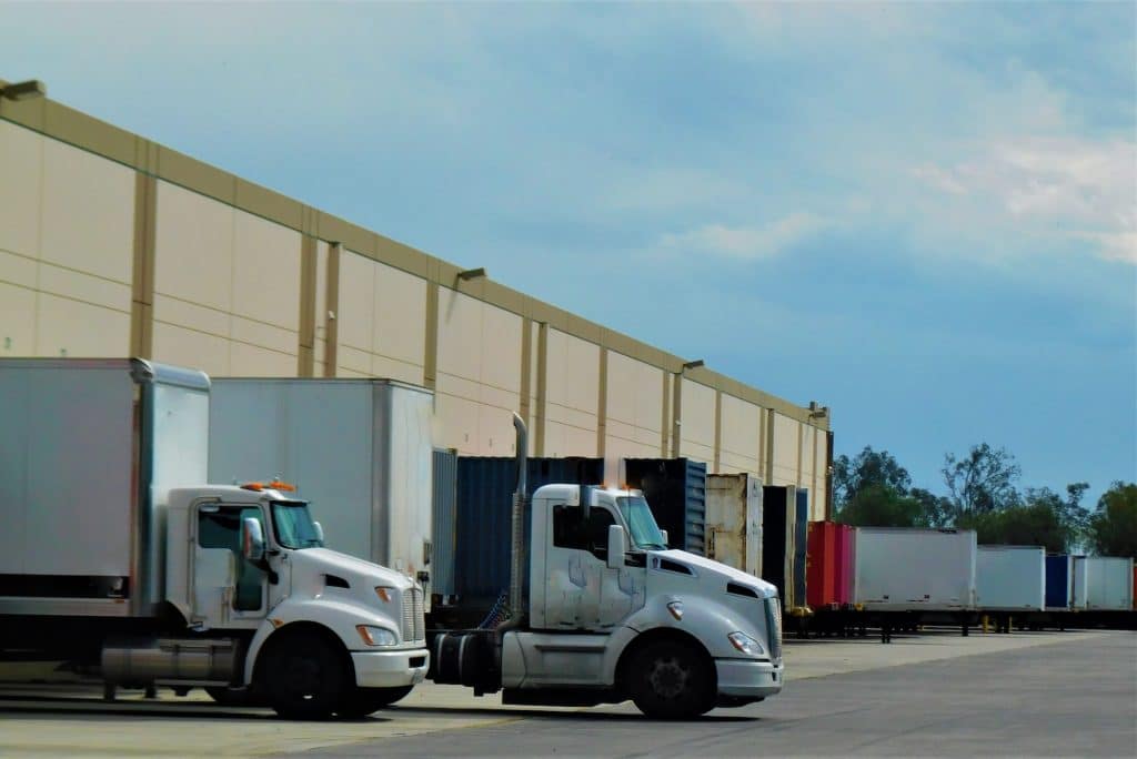 Large commercial trucks and trailers parked behind a warehouse distribution center.